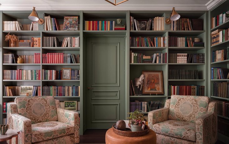 Green library with floor-to-ceiling bookshelves around a paneled door and two upholstered armchairs