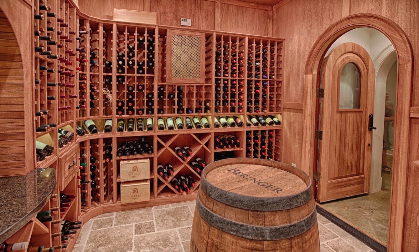 Walk-in wine cellar with wood racking, a stone floor, an arched wooden door and a barrel tasting table